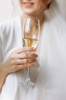 Gelinin sabahı. Gelin, Peignoir 'de şampanya içiyor. Genç bir kadın banyodaki bir otel odasında büyük bir pencerede oturuyor. Beyaz gelinlikli güzel kız. düğün günü.