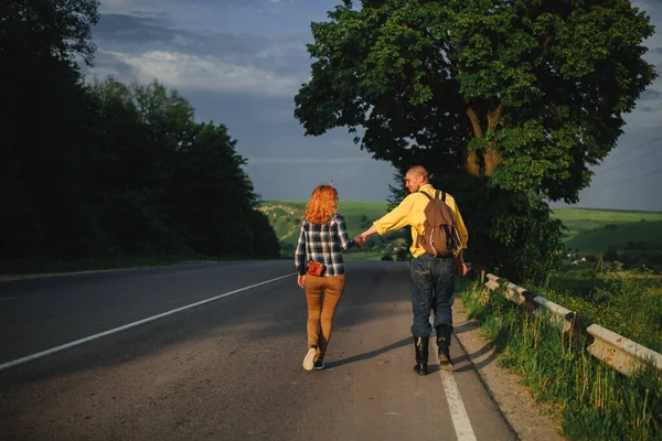 A man and a woman are hitchhiking. A young couple goes hitchhiking around the country. Free hitchhiking trip. A lover who travels free by hitchhiking. The couple goes traveling. Couple by the road.