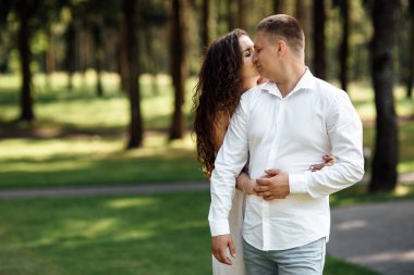 Genç aşık çift bir yaz günü parkta öpüşüyor. Erkek ve kadın dışarıda sarılıyorlar..