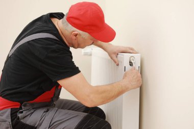 Odaya ısıtma radyatörü yerleştirirken İngiliz anahtarı kullanan işçi tulumu. Tesisatçı daireye ısıtma sistemi kuruyor. Radyatör kurulumu, tesisat işleri ve ev yenileme kavramı