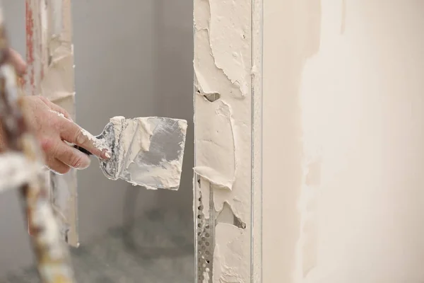 Builder using a trowel to add plaster. Plastering wall with putty-knife, close up image. Fixing wall surface and preparation for painting. construction work during quarantine.