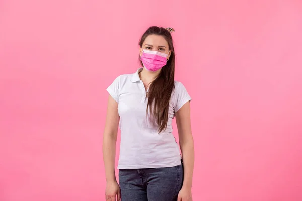 beautiful woman in pink medical mask on a pink background. woman wearing medical mask. protection against influenza virus. ear with protective face mask at home. stop coronavirus.