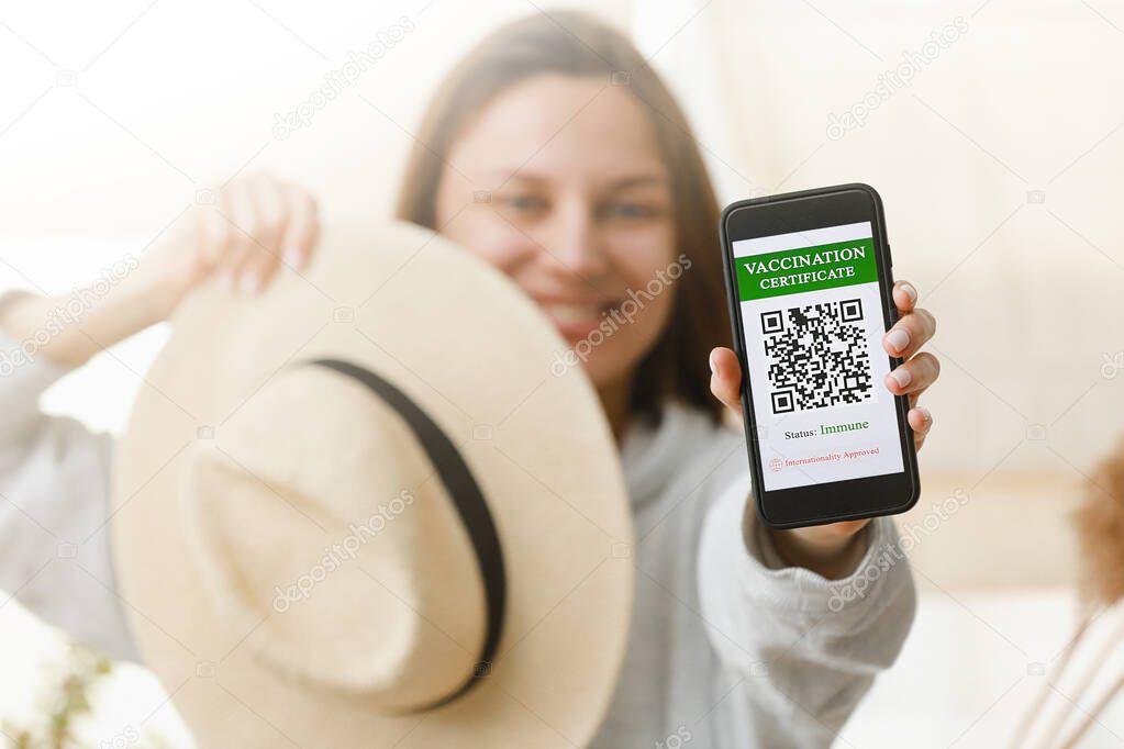 A defocused young girl is holding a passport and a smart phone with a certificate of vaccination against the Covid-19 disease. focus on the smart phone. Health Passport concept.