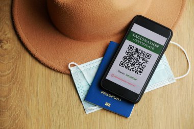 Yeni normal konsept. Bağışıklık sistemi dijital pasaportlu bir akıllı telefonun yakın görüntüsü. Ahşap arka planda, koruyucu maske, şapka ve pasaport.