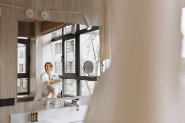Gelinin sabahı. Gelin, Peignoir 'de şampanya içiyor. Genç bir kadın banyodaki bir otel odasında büyük bir pencerede oturuyor. Beyaz gelinlikli güzel kız. düğün günü.