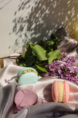 Pembe ve naneli Fransız kurabiyeleri veya badem kurabiyeleri ve kumaş arka planda leylak çiçekleri. Doğal meyve ve böğürtlen tatları, sevgililer günü için kremalı dolma anneler günü paskalyasında aşk yemeği..