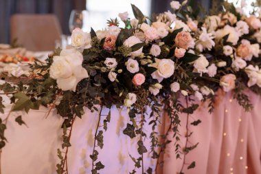 Düğün için. Ziyafet. Beyaz, pembe çiçekler ve yeşillik kompozisyonu ile dekore edilmiş misafirler için bir festival masası, restoranda servis edilen mumlar var..