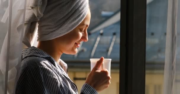 4 к. щаслива красива молода жінка з рушником на голові сніданок на балконі, пиття кави або чаю. дівчина дивиться на дахи міста вранці — стокове відео