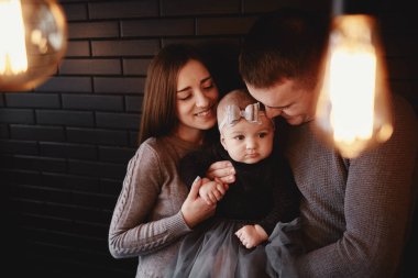 Genç bir ailenin portresi. Baba, anne ve bebek evde birlikte vakit geçiriyorlar. Ön planda retro ampuller var. Noel zamanı