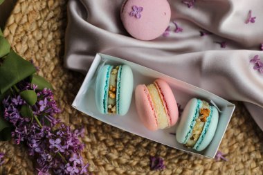 Pembe ve nane aromalı Fransız kurabiyeleri ya da hediye kutusunda kurabiyeler ve kumaş ve samanlıkta duran leylak çiçekleri. Doğal meyve ve böğürtlen tatları, sevgililer günü için kremalı dolma, Anneler Günü..