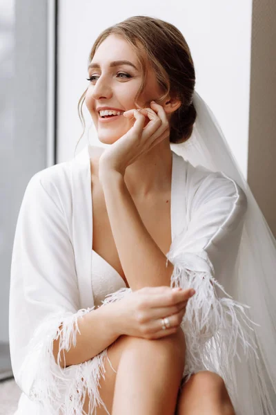花嫁の朝 豪華な花嫁だ 窓の白いローブに長い髪の美しい女性 結婚式の前の花嫁の朝 自然の美しさとプロの化粧 スキンケア製品 — ストック写真