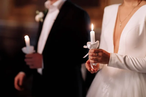 Couple in church. Bride and groom hold shiny candles during the ceremony in church. Hands of newlyweds with candles in church. Church religious details. Newlyweds swear to each other to love forever