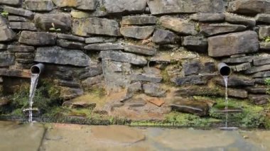 Ormandaki bir duvardan gelen iki metal borudan kaynak suyu dökülüyor.