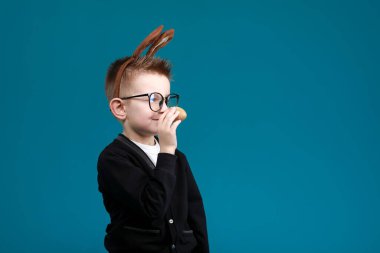Tavşan kulaklı neşeli çocuk mavi stüdyo arka planında kafası üzerinde. Heyecanlı, gülümseyen, gözlüklü mutlu çocuk. Yılın Paskalya mavisi rengi, ellerimle yumurta boyamak. Paskalya ve tatiller