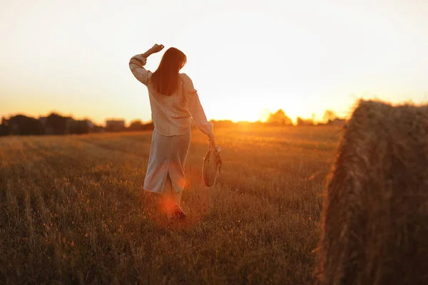 在美丽的夏日落日下的田野里 年轻女子正走在稻草包旁边 在野外长发的漂亮的浪漫女孩 — 图库照片