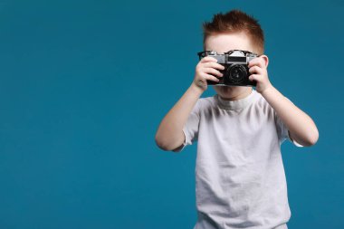 Küçük çocuk retro kamera kullanarak fotoğraf çekiyor. Klasik fotoğraf makinesi olan çocuk mavi arka planda izole edilmiş. Kopya uzayı ile eski teknoloji kavramı. Çocuk fotoğrafçılığı öğreniyor .