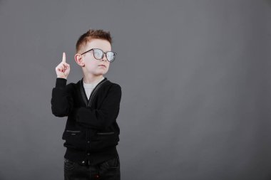 Parmağını kaldırmış şık küçük bir çocuğun portresi. Gözlüklü küçük çocuğun fikri var. Çocuk mavi karatahtada izole edilmiş. Başarı, parlak fikir, yaratıcı fikirler ve yenilik teknolojisi kavramı