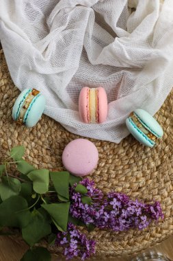 Pembe ve naneli Fransız kurabiyeleri ya da badem kurabiyeleri ve kumaş ve samanlıkta duran leylak çiçekleri. Doğal meyve ve böğürtlen tatları, kremalı dolma..