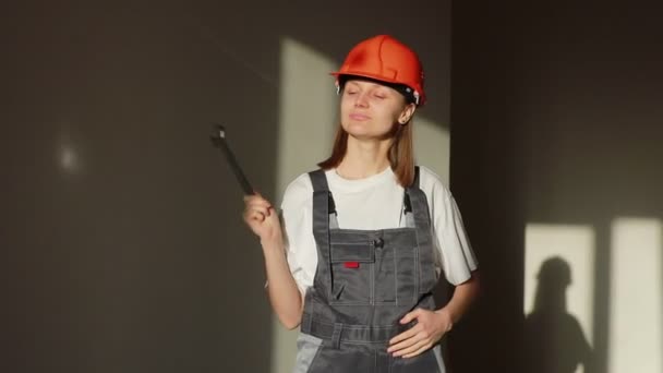 Portret młodej uśmiechniętej kobiety inżyniera lub budowniczego w kasku i kombinezonie pracującej na placu budowy lub fabryce i trzymającej klucz, odizolowanej na szarym tle — Wideo stockowe