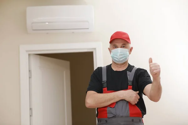 Work are done. Portrait of worker man with medical mask in red overall, black t shirt , red cap looking in camera and giving a thumbs up. white background, indoor studio shoot isolated.