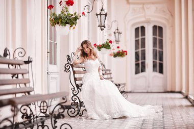 Güzel gelin, eski şehirde ahşap bankta oturuyor. Antik kentte dantel saten gelinlikli uzun saçlı genç bir kadın. Gülümse ve sev. düğün günü.