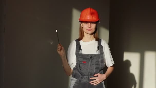 Portret van jonge lachende vrouwelijke ingenieur of bouwer in helm en jumpsuit werkend op fabrieks- of bouwplaats en met moersleutel, geïsoleerd over grijze achtergrond — Stockvideo