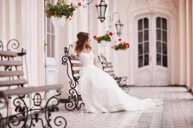 Güzel gelin, eski şehirde ahşap bankta oturuyor. Antik kentte dantel saten gelinlikli uzun saçlı genç bir kadın. Gülümse ve sev. düğün günü.