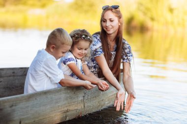 Genç ve güzel anne çocuklarla birlikte parkta gölde vakit geçiriyor. Anneler Günü. Kadınlar Günü 'nde. Oğlan ve kız su sıçrattı..