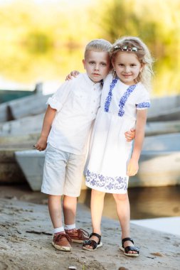Küçük kız ve oğlan, güneşli bir yaz gününde nehir kenarında oynuyorlar. Mutlu çocuklar nehirde yürüyüp su oynuyorlar. Çocuklar dışarıda oynuyorlar. Teknenin arkasında..