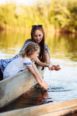 Genç ve güzel anne çocuklarla birlikte parkta gölde vakit geçiriyor. Anneler Günü. Kadınlar Günü 'nde. Oğlan ve kız su sıçrattı.