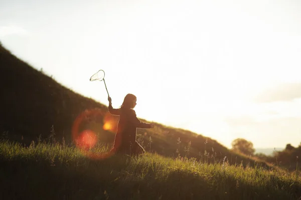 Little girl is walking with butterfly net and catching butterflies on the green hills on sunny summer day. copy space