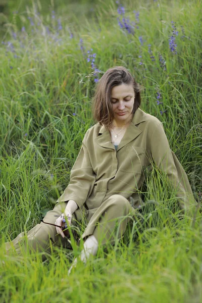 Portret van een jonge vrouw zittend in een veld op het lentegras tussen paarse bloemen. stijlvol meisje geniet van zonnig lenteweer. Natuurlijke schoonheid van een vrouw, natuurlijke cosmetica — Stockfoto