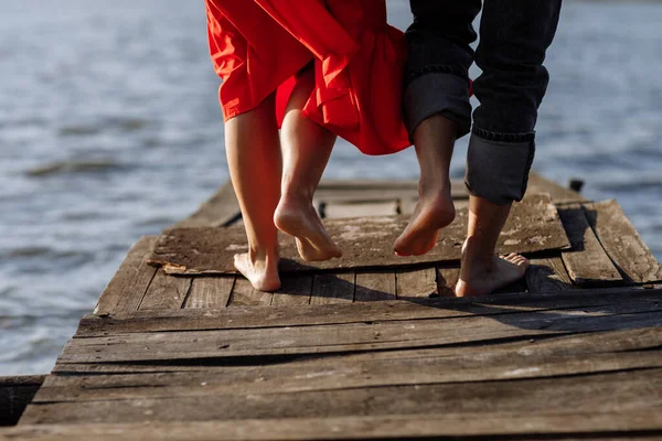 Gehakte foto jonge geliefden getrouwd stel, man en vrouw, vastgehouden van handen op een houten brug in de buurt van het meer. Achteraanzicht van het koppel dat op de pier staat. Onderste helft. Plaats voor tekst en ontwerp. Sluiten. — Stockfoto