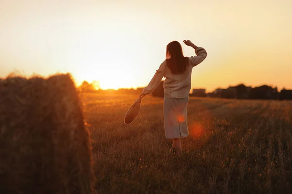 在美丽的夏日落日下的田野里 年轻女子正走在稻草包旁边 在野外长发的漂亮的浪漫女孩 — 图库照片