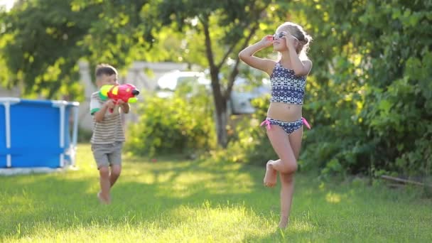 妹に水を撒き散らしてる 幸せな陽気な子供たちのスローモーションビデオ水銃で庭で楽しんで — ストック動画