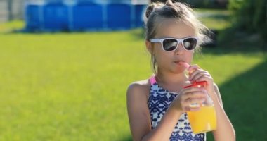 Güzel küçük kız, güneş gözlüklü mayo giyen tatlı çocuk portakal suyu içiyor. Çocuk havuz yakınındaki bir tatil köyünde eğleniyor. yaz tatili.