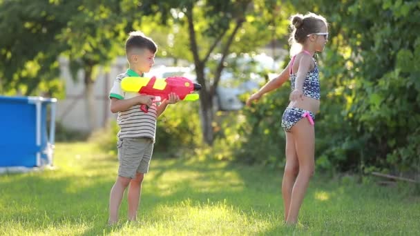 A kisfiú vizet fröcsköl a nővérére. Lassú mozgás videó boldog vidám gyerekek szórakozás kertben vízipisztollyal — Stock videók