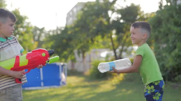 Két izgatott kisfiú vízipisztollyal játszik a kertben, a forró nyári napon, lassított felvételen. — Stock videók