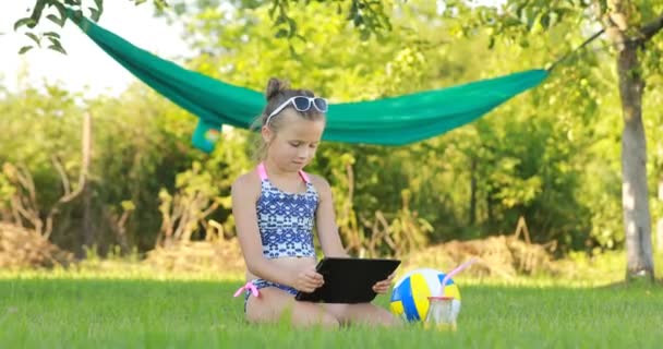 Menina em sunglasess está usando laptop e deitado na grama no verão dia ensolarado. rede e bola no fundo. férias de verão. — Vídeo de Stock