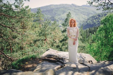 Ormanda, başında çiçekli bir çelenkle güzel, kızıl saçlı bir gelin. Yaz günü açık havada uzun beyaz elbiseli bir kadın. düğün günü.