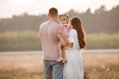 Mutlu bir ailenin portresi. Anne, baba ve kızı tarlada yürüyor. Genç bir aile tatilde, dışarıda birlikte vakit geçiriyor. Yaz tatili kavramı. Anneler günü, babalar günü, bebekler günü.