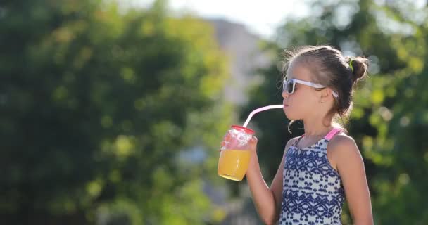Όμορφο κοριτσάκι, χαριτωμένο νήπιο σε μαγιό με γυαλιά ηλίου πίνει χυμό πορτοκάλι. Παιδί διασκεδάζει κατά τη διάρκεια των οικογενειακών διακοπών σε ένα θέρετρο κοντά στην πισίνα. καλοκαιρινές διακοπές — Αρχείο Βίντεο