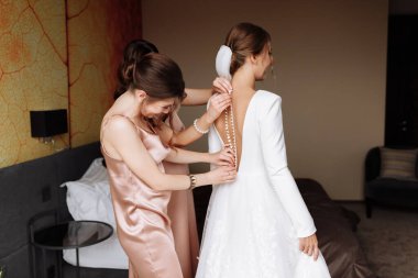 Nedimenin elleri gelinin düğmelerini takmasına yardım ediyor. Güzel beyaz bir dantelli elbisenin arkası düğmeli. Yakın plan, düğün günü için hazırlık konsepti.