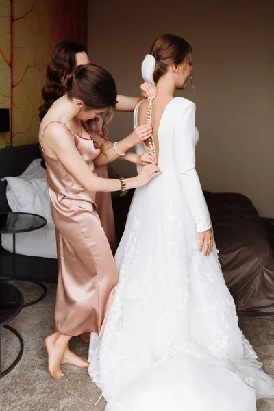 花嫁介添人の手を助ける花嫁は、美しい白いウェディングレースのヴィンテージドレスの後ろにボタンで締めくくり、結婚式の日の朝の準備コンセプト. — ストック写真