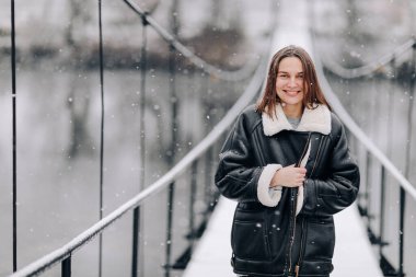 Bir kadın kış günü asma köprüde nehrin üzerinde yürüyor. Soğuk karlı bir günde, kalın elbiseli genç bir kız tahta bir yaya köprüsünde duruyor..