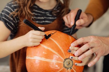 Mutlu aile sakallı baba Cadılar Bayramı 'nda evde anne ve çocuğuyla yemek yerken balkabağından balkabağı kabağı yapıyor.