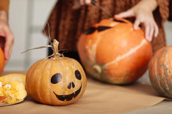 Close up of young woman carving Jack O Lattern from ripe orange pumpkin with knife on her wooden kitchen table. Female preparing all hallows eve Halloween party decorations. Background, copy space