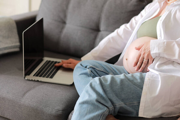 Attractive pregnant young lady working remotely online from home. Close up woman hands on laptop with big belly advanced pregnancy