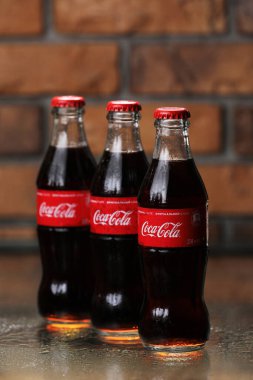 RIVNE, UKRAINE 26 HAZİRAN 2020: tuğla duvar arkasında üç klasik Coca-Cola şişesi. Coca-Cola kutuları.