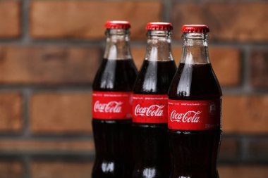 RIVNE, UKRAINE 26 HAZİRAN 2020: tuğla duvar arkasında üç klasik Coca-Cola şişesi. Coca-Cola kutuları.